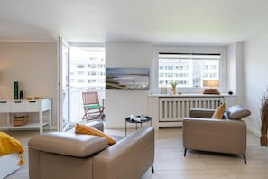 A modern living room with a sofa, armchair, and a dining table with chairs. - Holiday apartment with 1 bedroom (Westerland)
