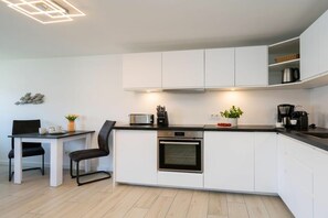 A modern kitchen with white cabinets, a built-in oven, a coffee machine, and a dining area with a table and chairs. - Holiday apartment with 1 bedroom (Westerland)