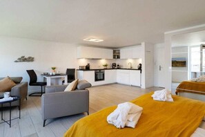 A modern hotel room with a sofa, a bed with towels, a small kitchen area, and a dining table. - Holiday apartment with 1 bedroom (Westerland)