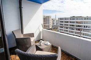 Ein Balkon mit Korbmöbeln und einem Tisch, mit Blick auf eine Skyline mit mehreren Gebäuden.