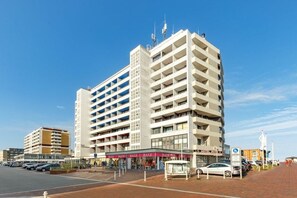 Ein mehrgeschossiges Hotel mit einem zentralen Atrium, einem Parkplatz und blauem Himmel.