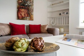 A living room with a sofa, red cushions, a table with an open magazine, and a decorative piece on the wall. - Holiday apartment with 1 bedroom (Westerland)
