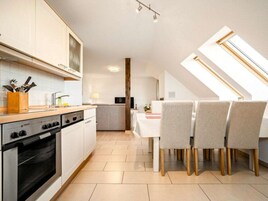 Cozinha moderna com forno embutido, espaço de refeições com mesa e cadeiras, e claraboias.