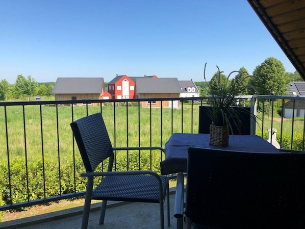 Varanda com mesa e cadeiras, com vista para um gramado e casas.