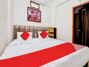 Une chambre d’hôtel avec un lit, une tête de lit en bois, une couvre-lit rouge et blanche, et un tableau encadré accroché au mur.
