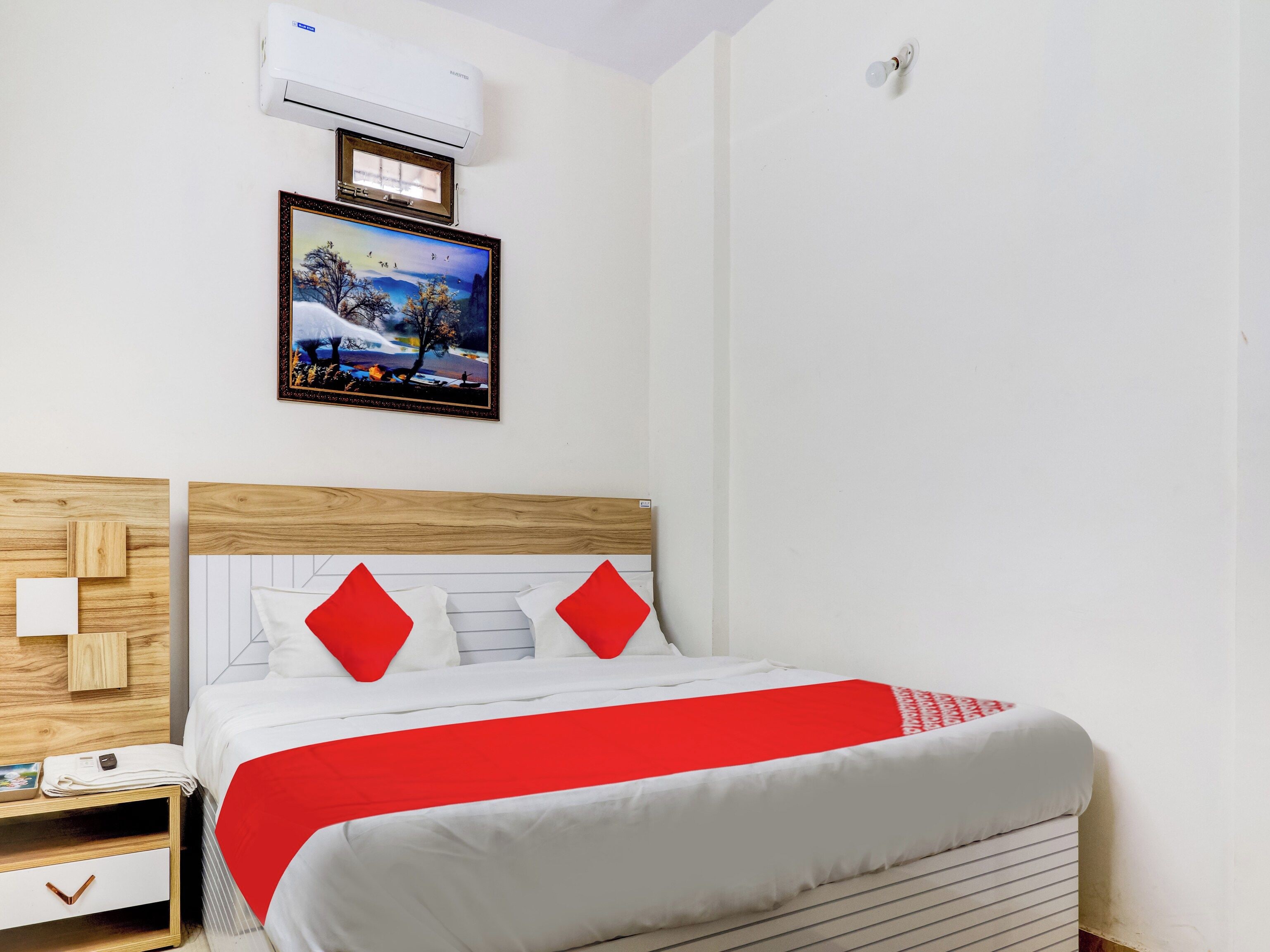 A bedroom with a bed, a nightstand, a framed picture, and an air conditioning unit.