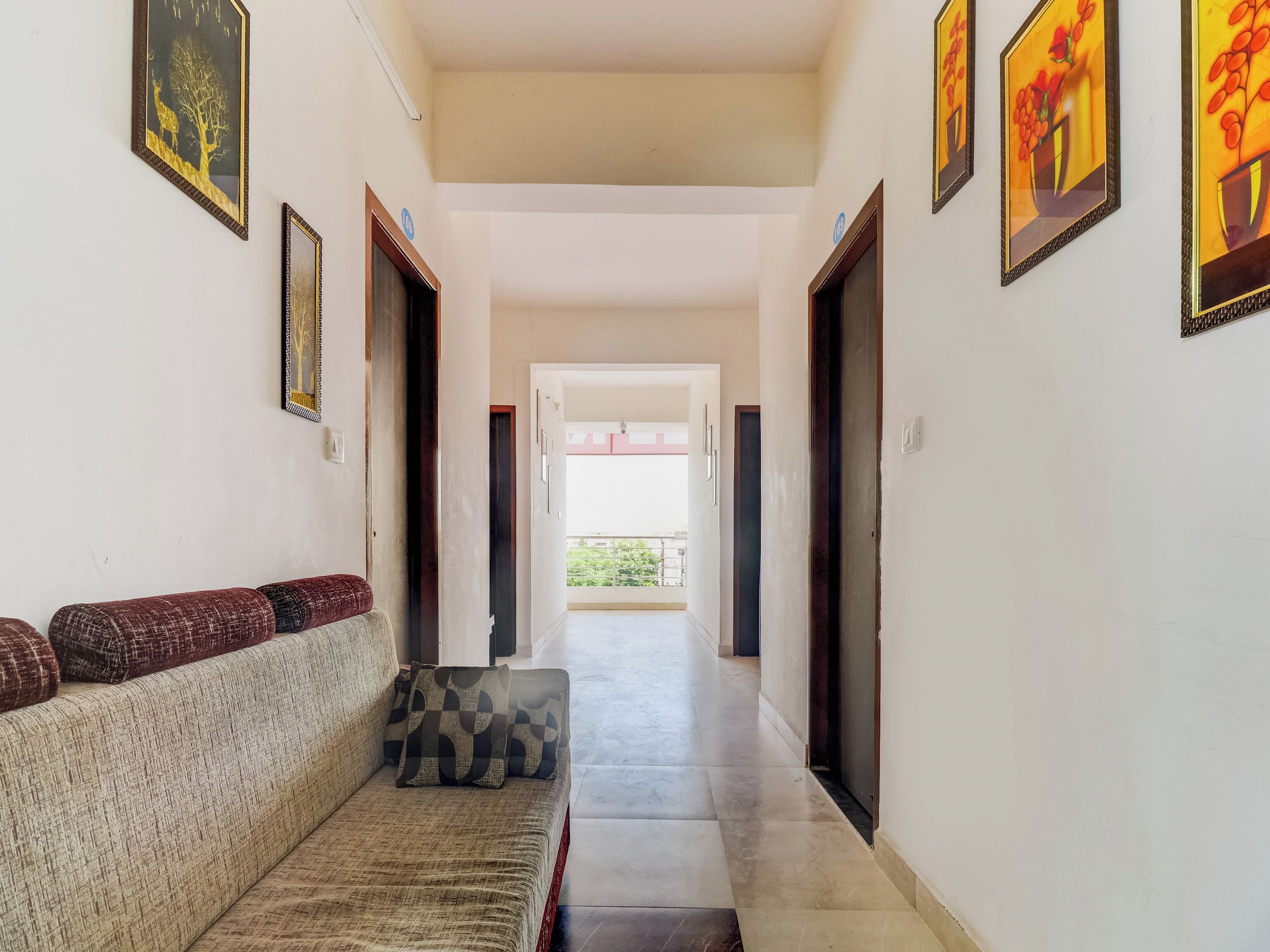 A hallway with a sofa and a bench, framed artwork on the walls, and doors leading to other rooms.