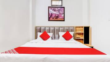 Una cama con una colcha blanca y roja, dos almohadas rojas y un cabecero de madera.