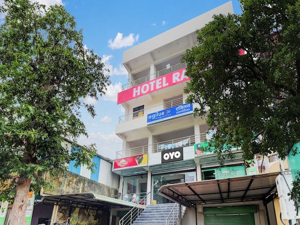 Un immeuble à plusieurs étages, sur lequel on peut voir une grande enseigne « HÔTEL RA », une autre indiquant « Les meilleures villes » et une entrée arborant le logo « OYO ».