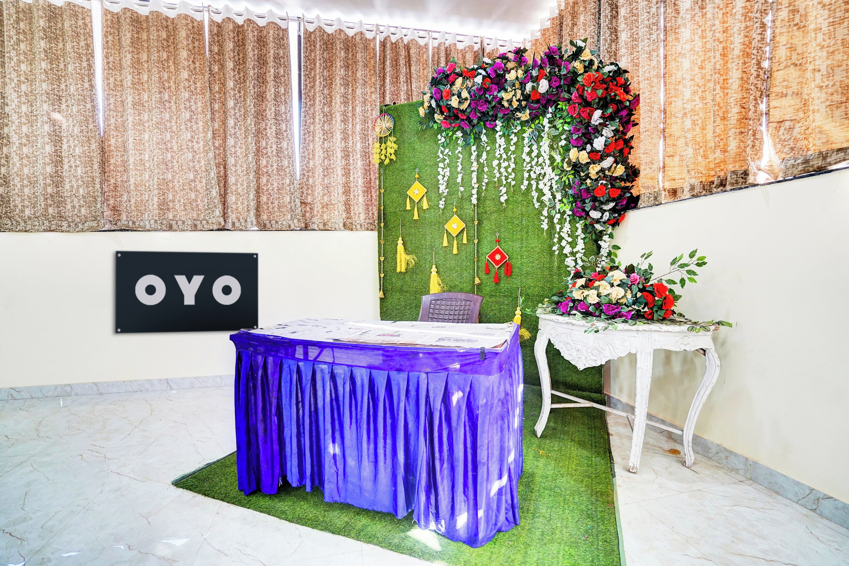 A room with a table covered in a blue cloth, a sign with 'OYO' on the wall, and a floral arrangement on the wall.