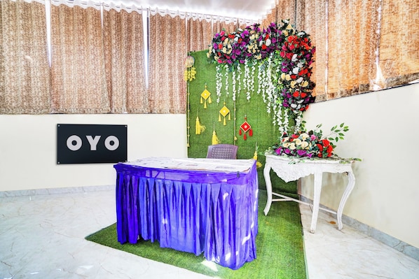A room with a table covered in a blue cloth, a sign with 'OYO' on the wall, and a floral arrangement on the wall. - Hotel O Godavari Lawn (Jabalpur)