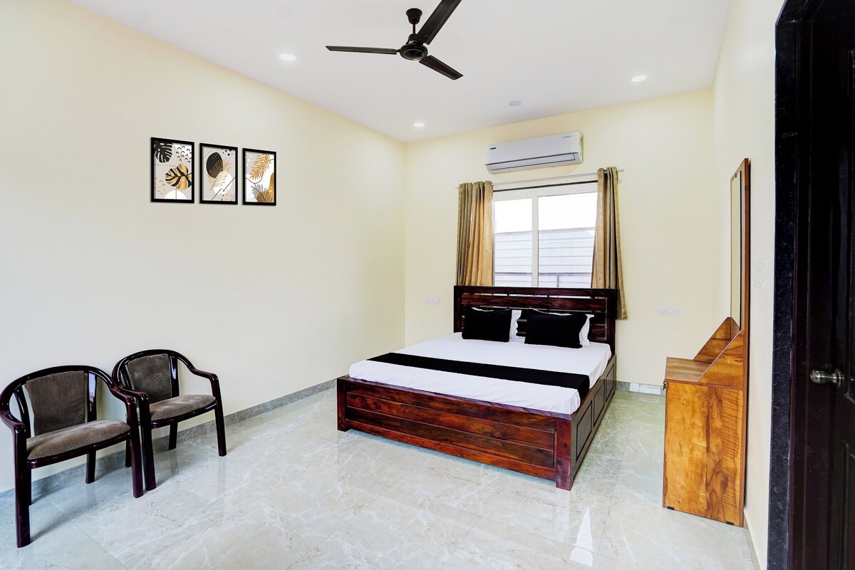 A bedroom with a bed, a chair, a ceiling fan, an air conditioning unit, and a window with curtains.
