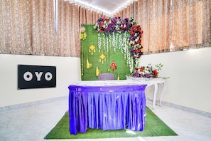 A room with a table covered in a blue cloth, a green wall with hanging decorations, and a sign with 'OYO' on it.
