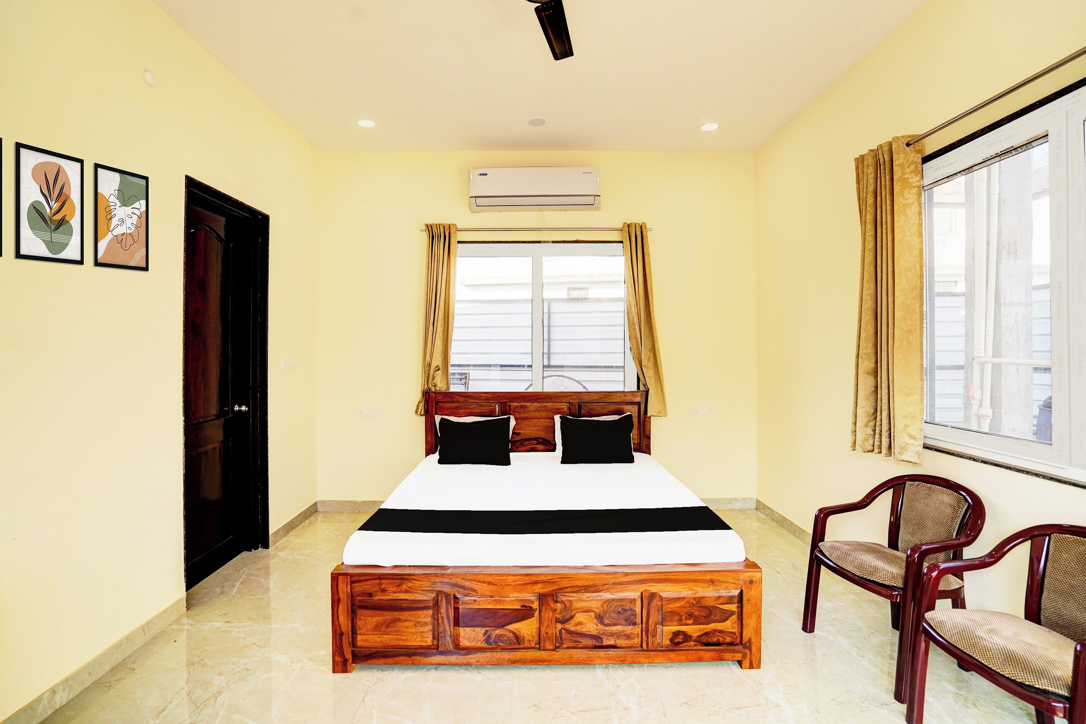 A hotel room with a bed, a window with curtains, a chair, and an air conditioning unit.