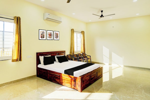 A hotel room with a wooden bed, a ceiling fan, an air conditioning unit, and framed artwork on the wall.
