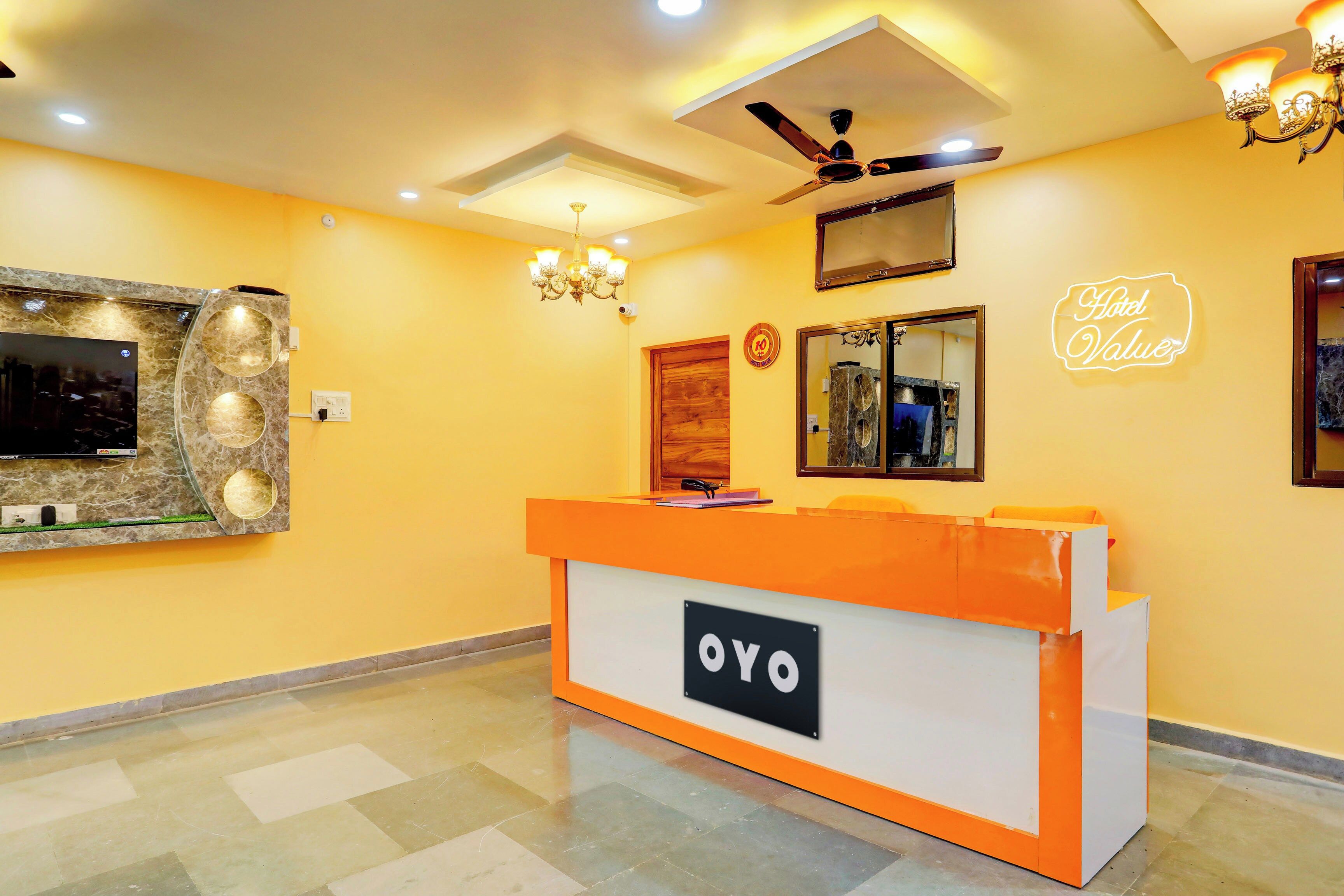 En receptionsdisk med en skylt som visar texten ”OYO” i en hotellobby med en gul vägg, en takfläkt och en kristallkrona.