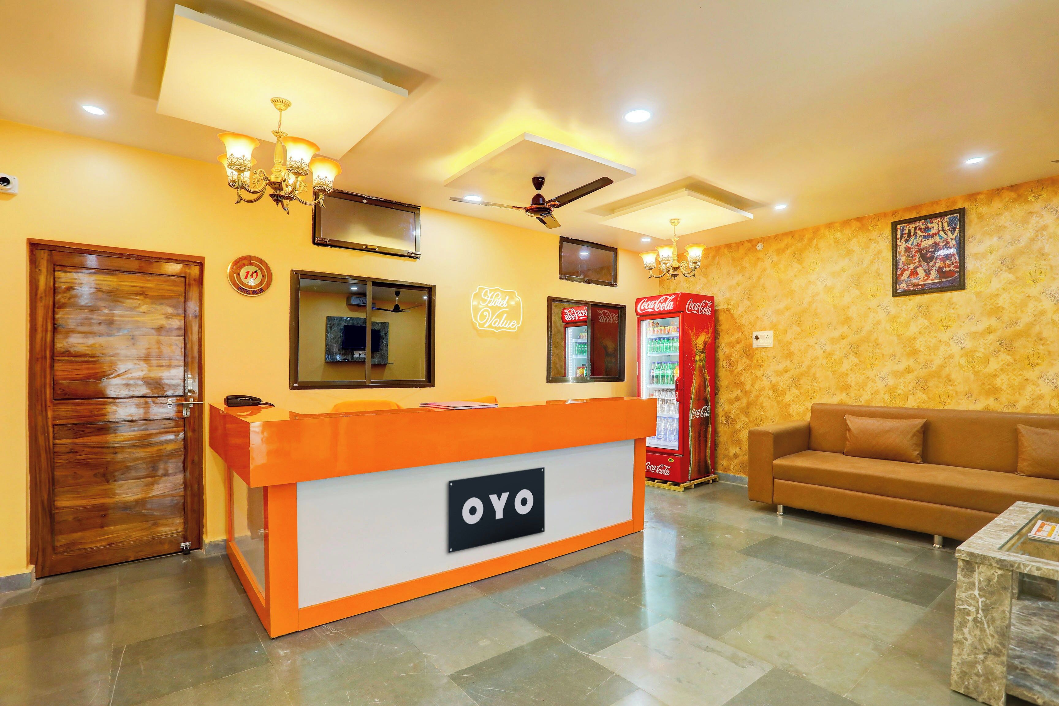 A hotel reception area with a reception desk, a sofa, a Coca-Cola refrigerator, and a ceiling fan.