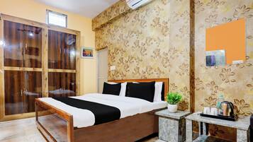 A hotel room with a wooden bed, a small bedside table, a potted plant, and a wall-mounted air conditioner.