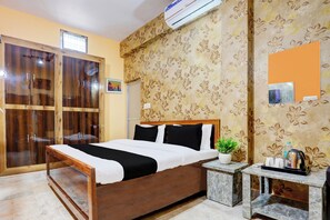Une chambre d’hôtel avec un lit en bois, une petite table de chevet, une plante en pot et un climatiseur fixé au mur.