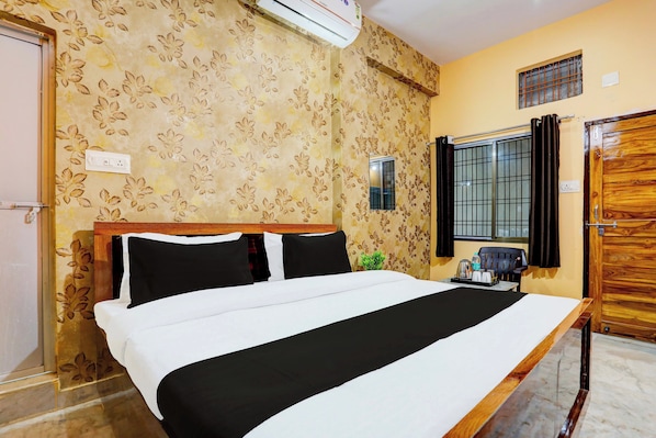 A hotel room with a bed, a window with bars, a wall-mounted air conditioner, and a wooden door. - Hotel O by OYO Value (Jabalpur)