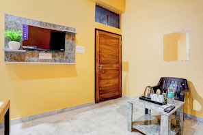 A room with a marble floor, a wooden door, a television mounted on a marble wall, a small table with a tray, and a chair. - Hotel O by OYO Value (Jabalpur)