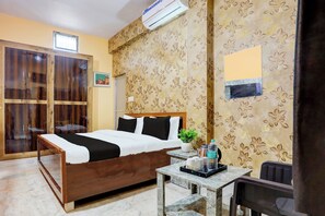 Une chambre d’hôtel avec un lit en bois, une petite table sur laquelle se trouve une plante, une bouteille d’eau et un radiateur.