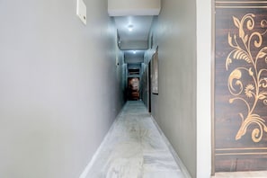 A narrow hallway with a marble floor, light-colored walls, and a decorative door on the right. - Hotel O by OYO Value (Jabalpur)