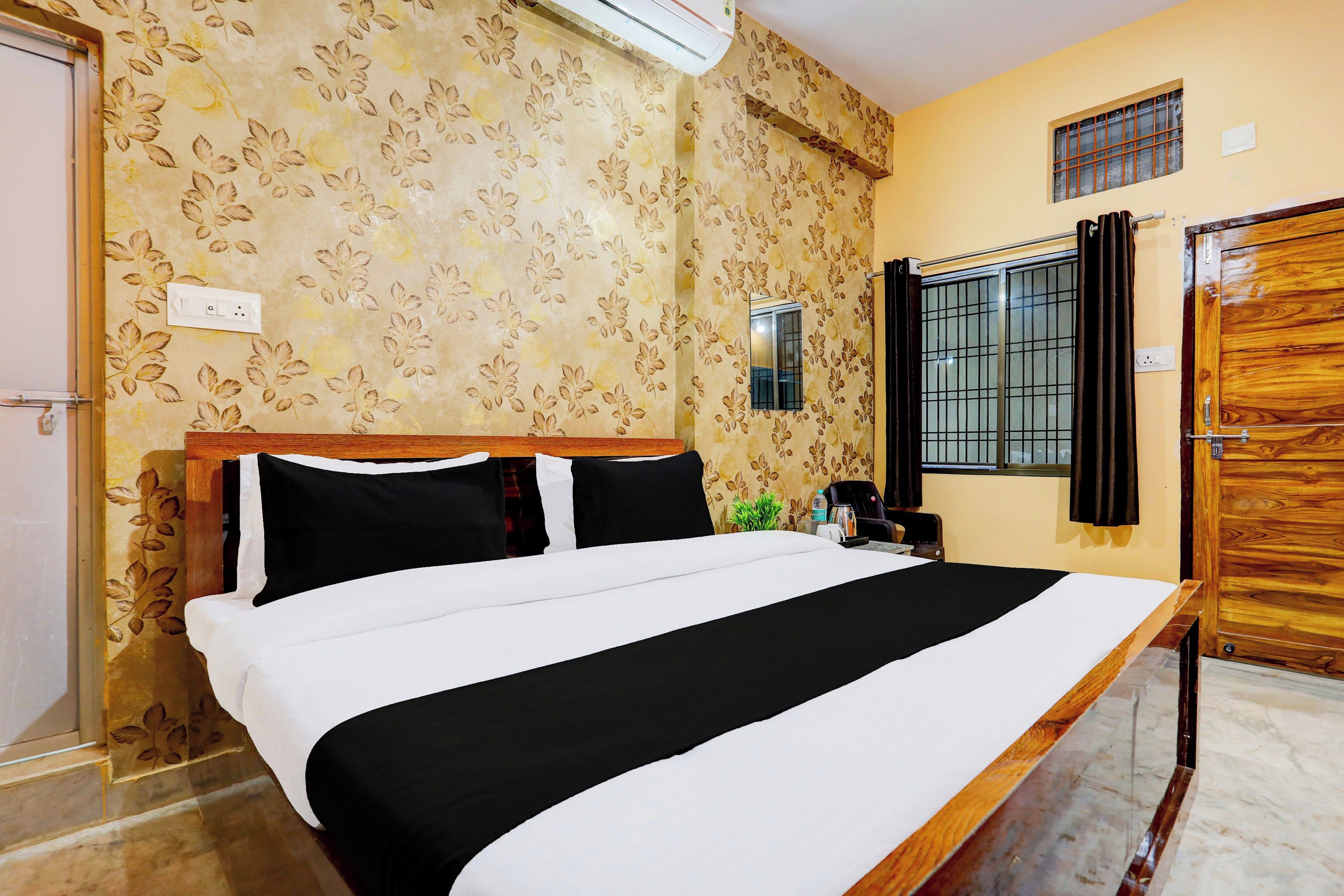 Une chambre d’hôtel avec un lit, une petite table avec une bouilloire, une fenêtre avec des rideaux et une porte.