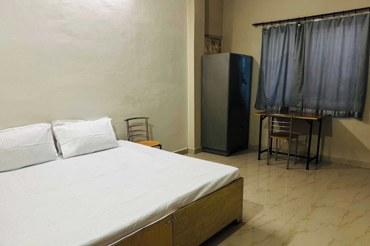 A bedroom with a bed, a small table, a chair, a wardrobe, and a window with curtains.