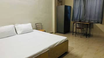 Une chambre à coucher avec un lit, une petite table, une chaise, une armoire et une fenêtre avec des rideaux.