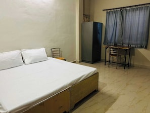 Une chambre à coucher avec un lit, une petite table, une chaise, une armoire et une fenêtre avec des rideaux.