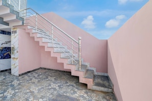 A staircase with a metal handrail leading to a landing, surrounded by pink walls and a tiled floor. - Hotel O by OYO Virashat (Sihora)
