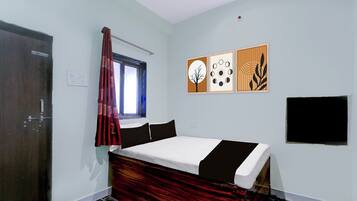 A bedroom with a bed, a window with curtains, a wall-mounted TV, and three framed artworks.
