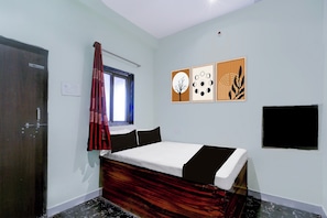 Une chambre à coucher avec un lit, une fenêtre avec des rideaux, un téléviseur fixé au mur et trois œuvres d’art encadrées.