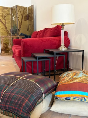 A room with a red sofa, a small table, and two patterned cushions. - New Listing (Roma)