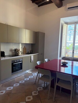 A kitchen with a built-in oven, a dining table with chairs, and a window with a view of buildings. - New Listing (Roma)