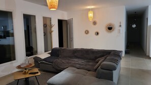 A living room with a grey sofa, a coffee table, and a TV. There are decorative wall mirrors and a ceiling light fixture. - New Listing (Roujan)