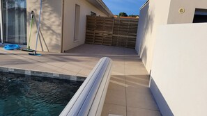Piscina com deck revestido em azulejo, cerca de madeira e materiais de limpeza.