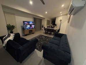 A living room with a flat-screen TV, two sofas, a dining table with chairs, and a potted plant. - Luxurious family home away from home, comfortable (Park Ridge)