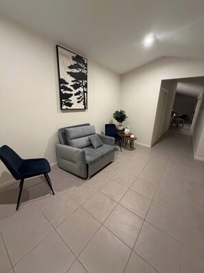 A living room with a grey sofa, a blue chair, a small table with a plant, and a framed artwork on the wall. - Luxurious family home away from home, comfortable (Park Ridge)