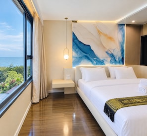 A hotel room with a large bed, a bedside table, a nightstand, a wall-mounted lamp, and a view of the sea. - Private and Direct access to the beach in Pattaya Jomtien (Pattaya Jomtien)