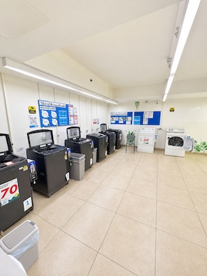 A laundry facility with multiple washing machines and dryers, numbered signs, and instructional posters on the walls. - Prime Location Apartment in Pattaya Jomtien (ตำบล หนองปรือ)