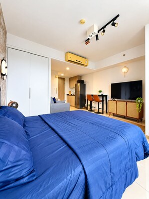 A modern bedroom with a large bed, a kitchenette, and a TV. - Prime Location Apartment in Pattaya Jomtien (ตำบล หนองปรือ)