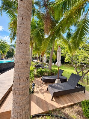 A poolside area with lounge chairs and umbrellas, surrounded by palm trees and greenery. - Prime Location Apartment in Pattaya Jomtien (ตำบล หนองปรือ)