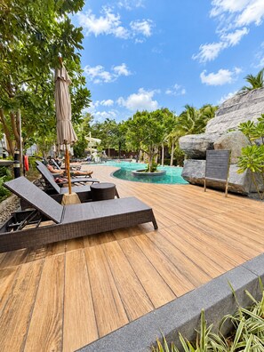 A wooden deck with lounge chairs and a pool area, surrounded by tropical plants and a large rock formation. - Prime Location Apartment in Pattaya Jomtien (ตำบล หนองปรือ)