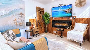 Ein modernes Wohnzimmer mit großem Fernseher, Kamin und Wandgemälde mit Strandmotiv.