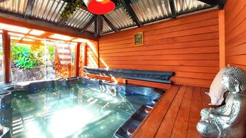 A hot tub with a wooden bench and a Buddha statue, surrounded by wooden walls and a metal roof.