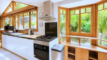 A modern kitchen with a central island, a stove, and a built-in oven. Large windows provide views of greenery outside.