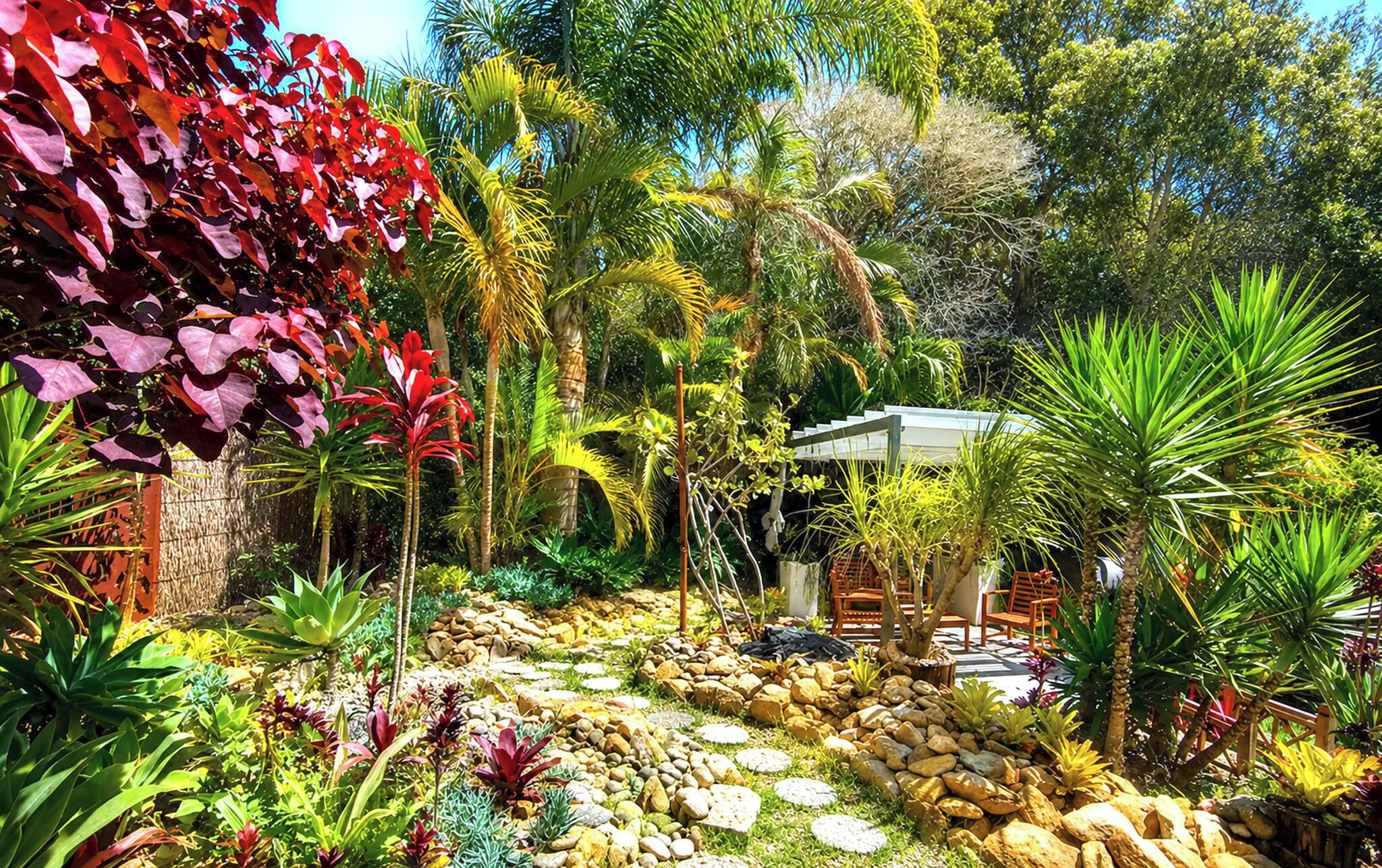 A garden with a variety of plants, a gazebo, and a seating area with chairs.