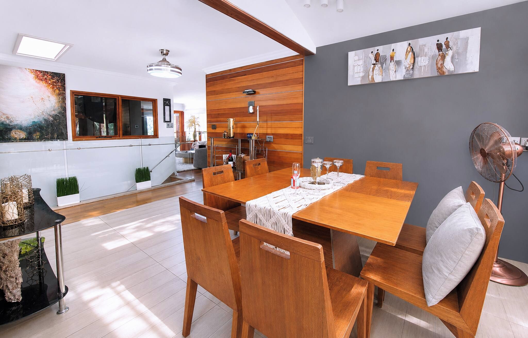 Un coin repas avec une table et des chaises en bois, un ventilateur de plafond et un tableau accroché au mur.